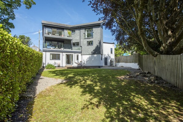 A modern two-story house with a balcony, a well-maintained lawn, and a wooden fence.