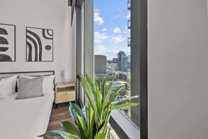 Ein modernes Schlafzimmer mit Blick auf die Stadt, ein Bett, ein Nachttisch und eine Topfpflanze.