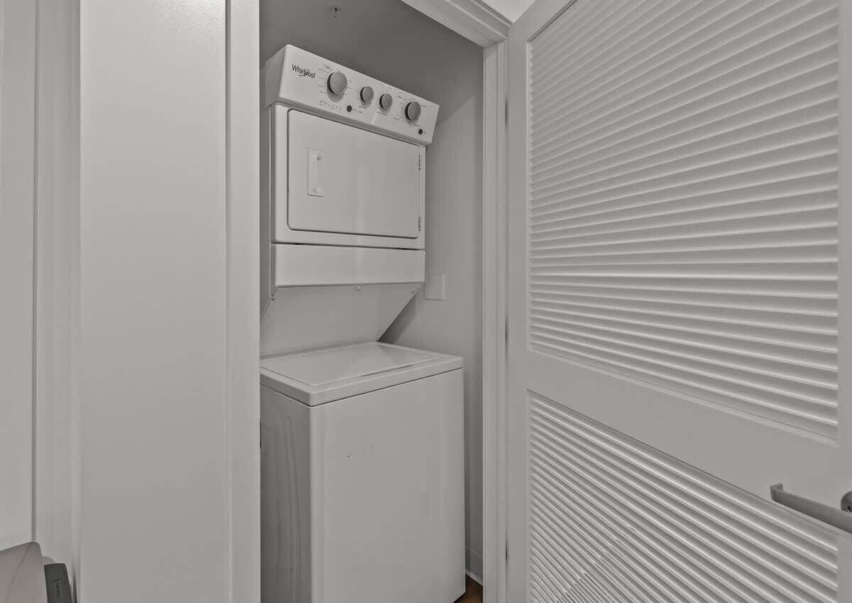 Une petite buanderie équipée d’un lave-linge et d’un sèche-linge à chargement frontal, d’une porte blanche à panneaux horizontaux et d’un plafond blanc.