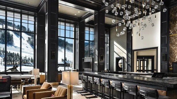 A modern bar area with a long counter, bar stools, and large windows offering a view of a snowy mountain. - Ski-in/Ski-out Park Hyatt Beaver Creek | Luxury Double Villa (Avon)