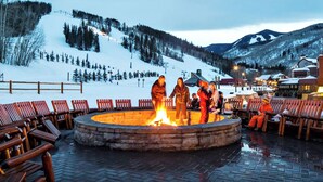 A circular stone fire pit surrounded by wooden benches, with a snowy mountain backdrop. - Ski-in/Ski-out Park Hyatt Beaver Creek | Luxury Double Villa (Avon)