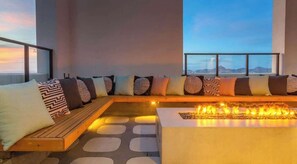 A modern lounge area with a fire feature, seating with patterned cushions, and a view through large windows. - Boulevard Stays Modern Highrise STU Sky Pool, Gym 11 (Phoenix)