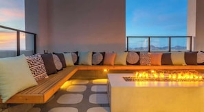 Ein moderner Loungebereich mit Kamin und Sitzgelegenheiten, ausgestattet mit gemusterten Kissen, und Blick durch große Fenster.
