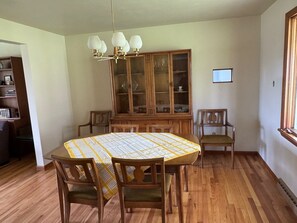 A dining room with a wooden table, chairs, a chandelier, a wooden cabinet, and a window. - NFL ready 30 min from stadium Charming 3-bedroom bungalow Harrison City (harrison city)