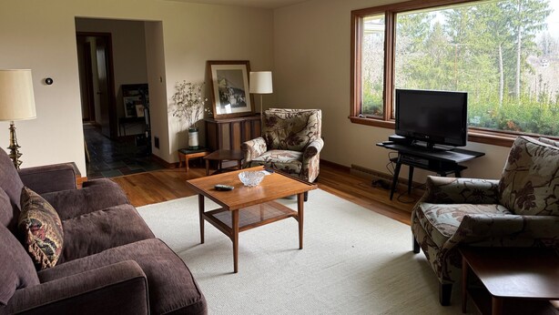 A living room with a sofa, armchair, coffee table, TV, and a window with a view of trees. - NFL ready 30 min from stadium Charming 3-bedroom bungalow Harrison City (harrison city)