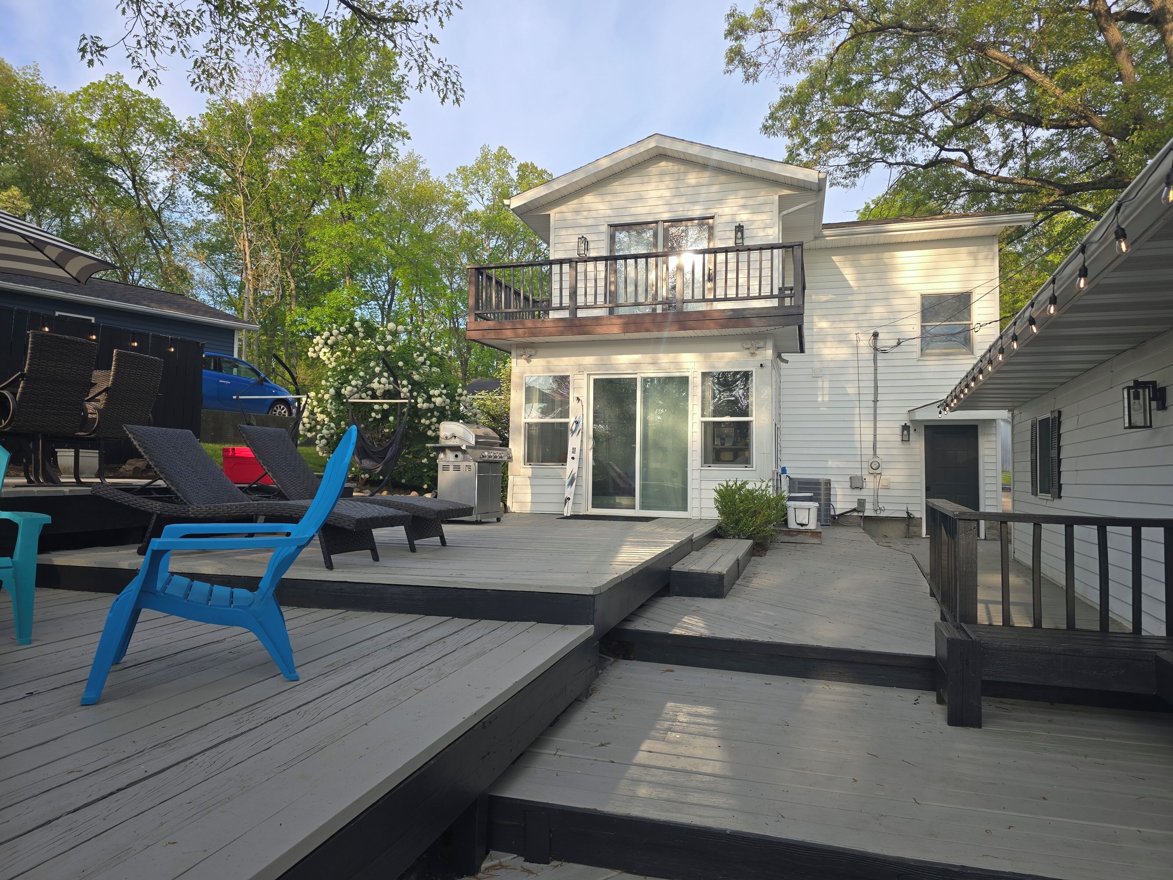 A deck with outdoor furniture, a barbecue grill, and a two-story house with a balcony.