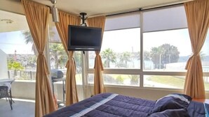 Un dormitorio con cama, televisión y balcón con cortinas.