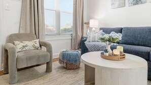 A living room with a beige armchair, a blue sofa, a round coffee table, and a window with curtains. - Stylish 3-bedroom Escape in charming Alexandria 5 Min to Old Town, Metro Nearby (Alexandria)
