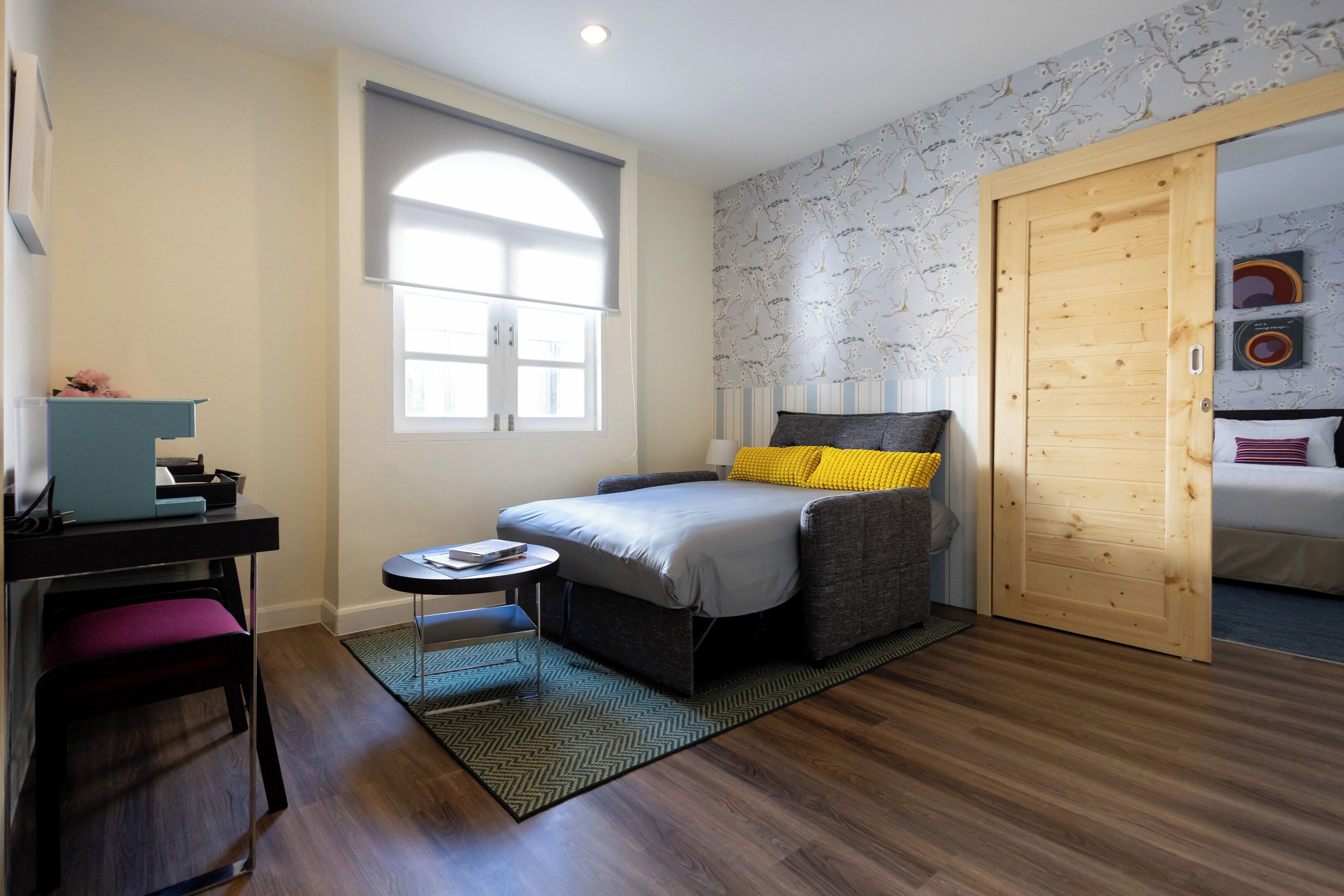 A bedroom with a bed, a desk, a chair, a window, and a door.