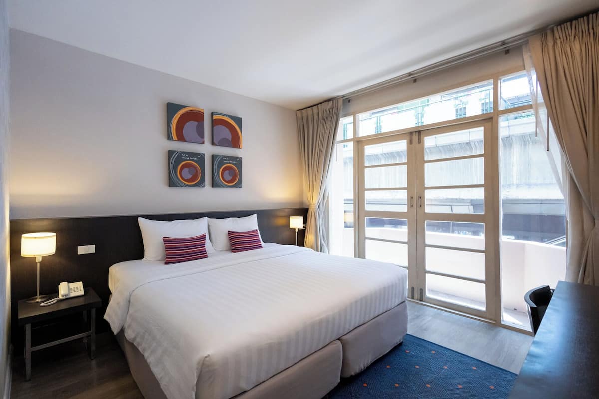Ein Hotelzimmer mit einem großen Bett, zwei Nachttischen, einem Schreibtisch und einem großen Fenster mit Vorhängen.