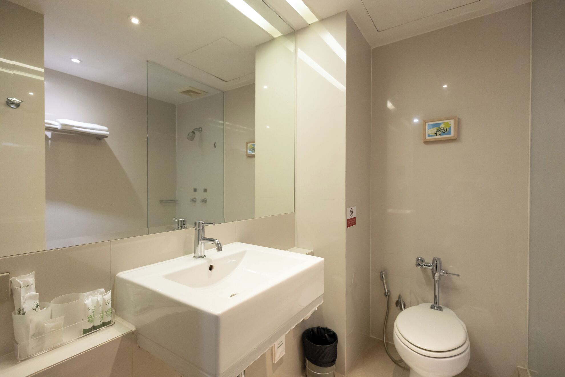 A modern bathroom with a large mirror, a white sink, a toilet, and a shower.
