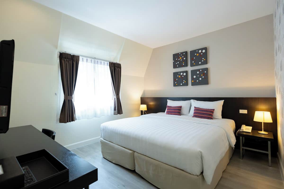 Ein Hotelzimmer mit einem großen Bett, einem Schreibtisch, einem Stuhl, einem Nachttisch mit Lampe und einem Bild an der Wand.