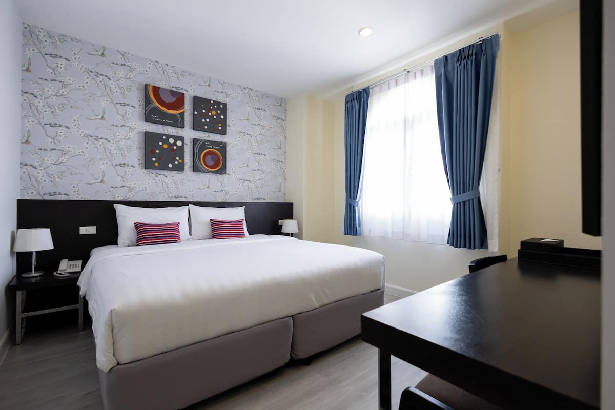 Ein Hotelzimmer mit einem großen Bett, einem Schreibtisch, einem Nachttisch und einer Wand mit Kunstwerken.