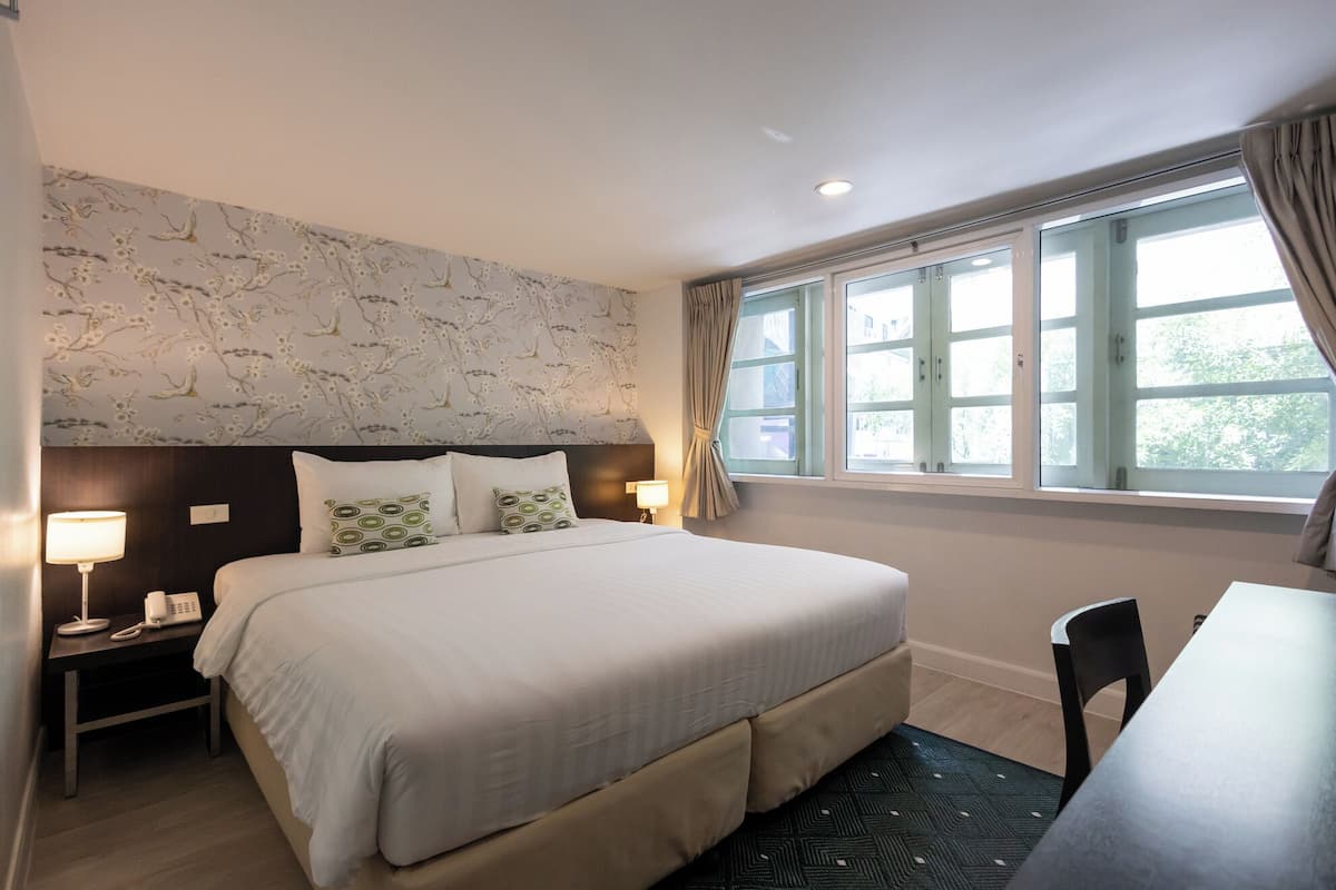 Ein Hotelzimmer mit einem großen Bett, Nachttischlampen, einem Schreibtisch und einem Fenster mit Vorhängen.