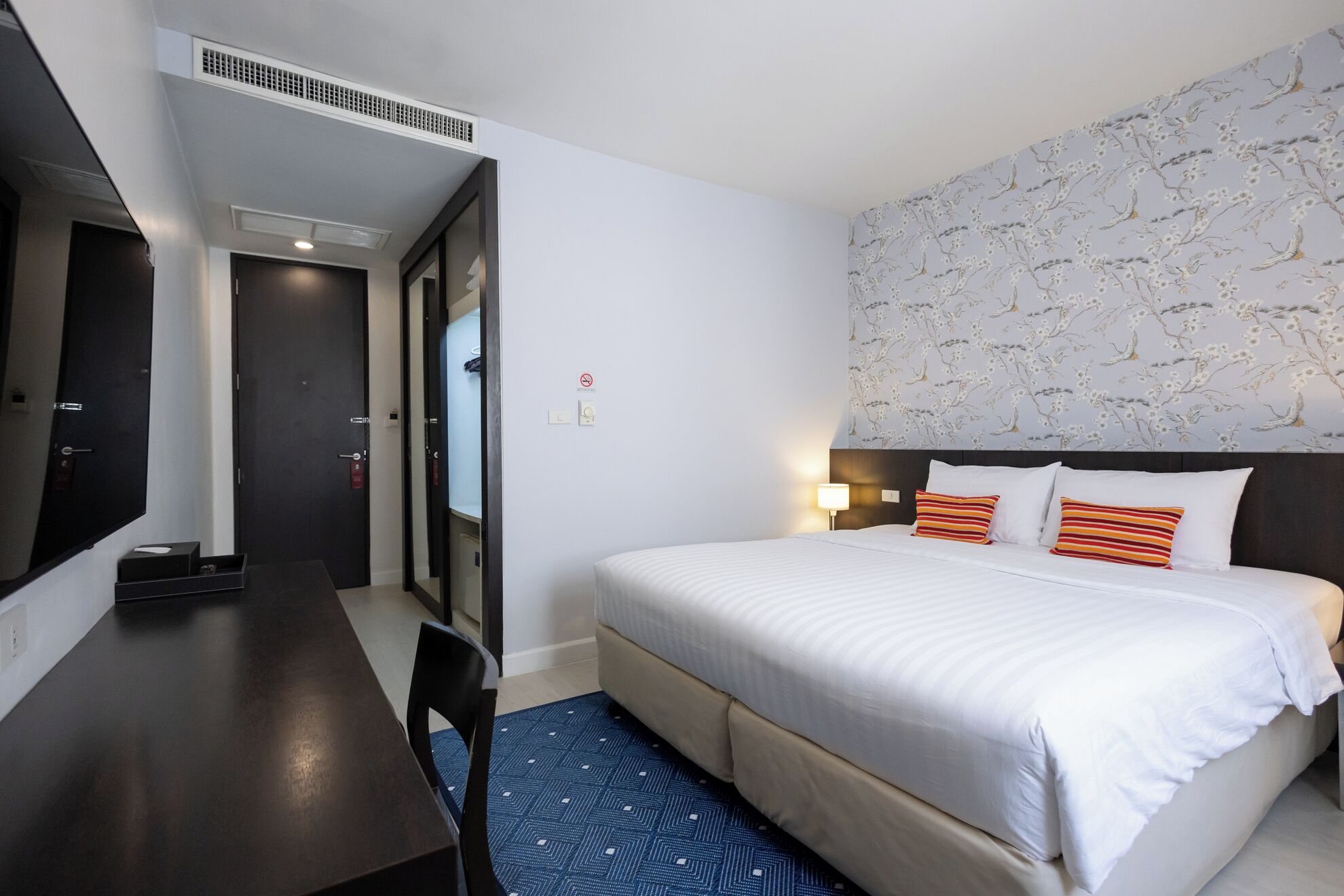 A hotel room with a bed, a desk, and a mirror.