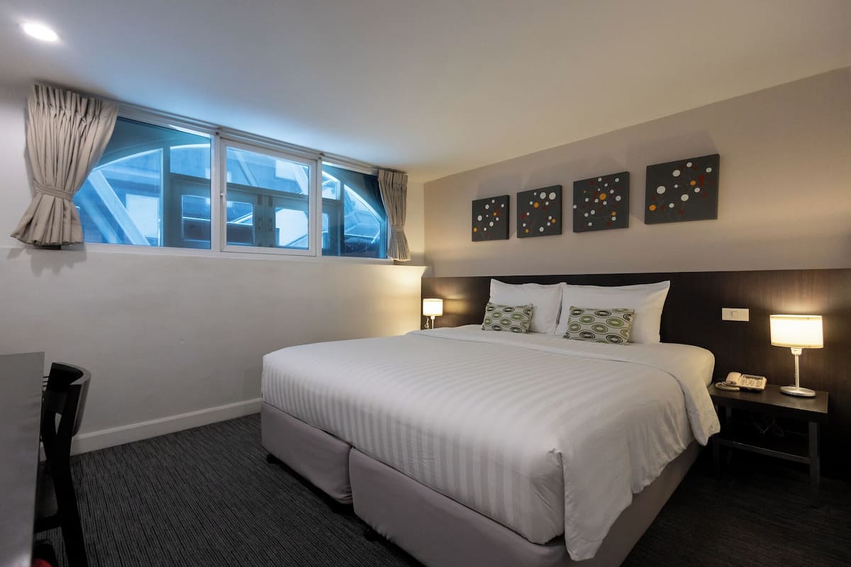 Ein Hotelzimmer mit einem großen Bett, zwei Nachttischen, einem Schreibtisch und einem Fenster mit Vorhängen.
