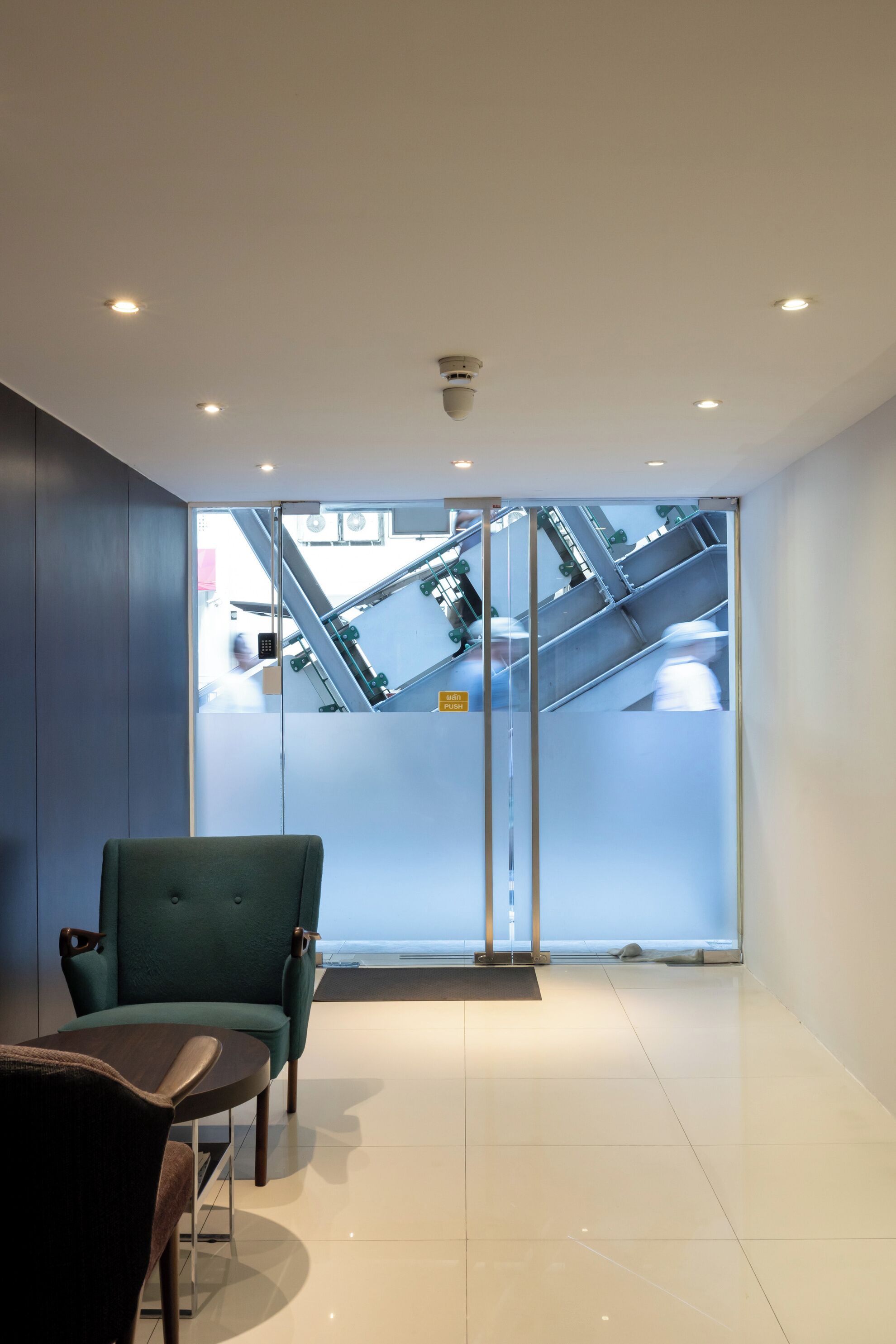 Un interior moderno con una silla tapizada de verde, una mesa de madera y vistas a una escalera mecánica.