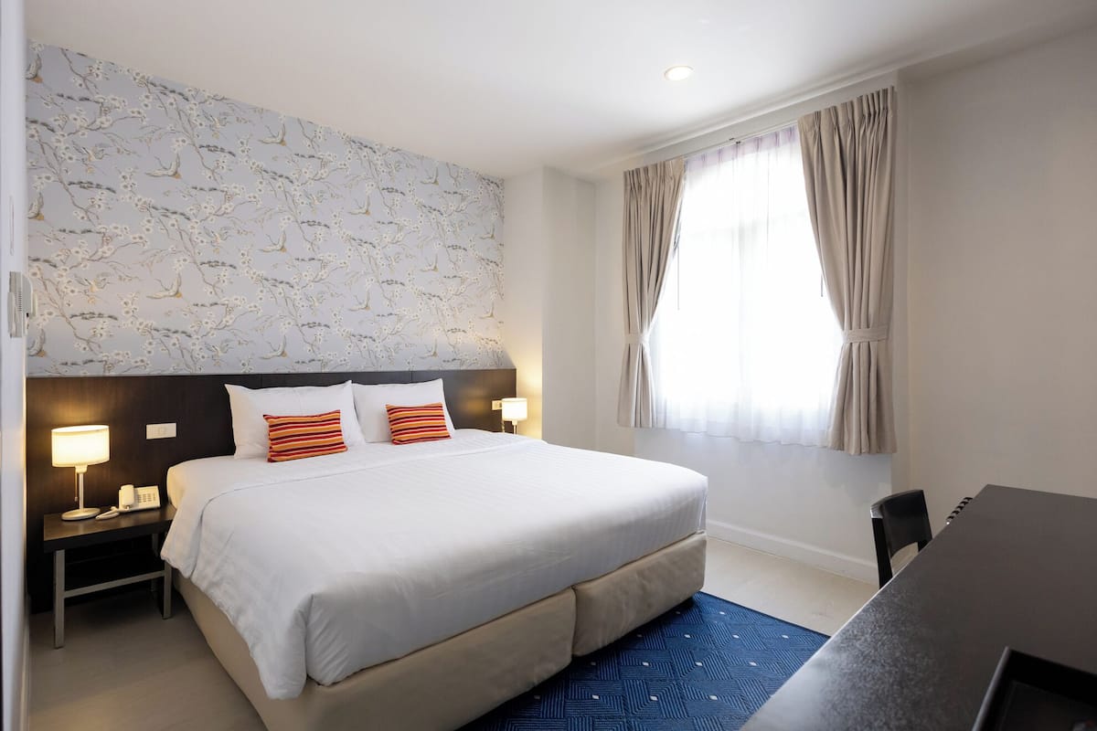 Ein Hotelzimmer mit einem großen Bett, zwei Nachttischen mit Lampen, einem Schreibtisch und einem Fenster mit Vorhängen.