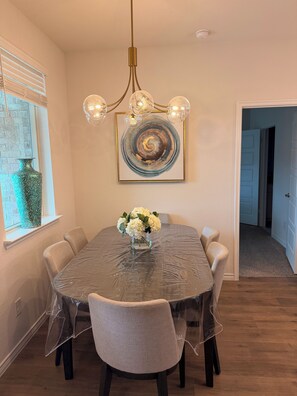 A dining room with a round table, six chairs, a chandelier, and a framed abstract painting.