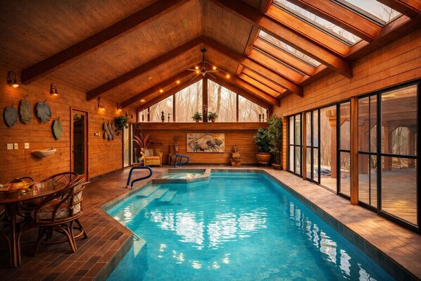 An indoor swimming pool with wooden walls and a sloped ceiling, surrounded by large windows and potted plants.