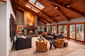 A spacious living room with a fireplace, large windows, and a high ceiling.