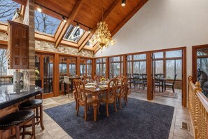 A spacious dining area with a large table, wooden chairs, and a chandelier.