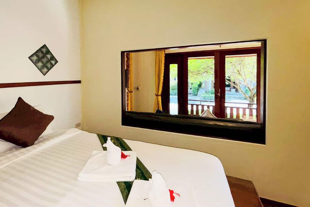 A hotel room with a bed, pillows, a window with a view of the outdoors, and two wall-mounted decorative items.