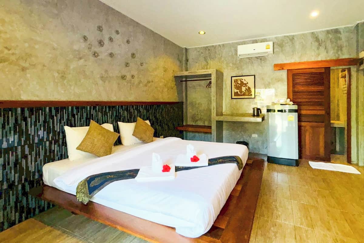 A hotel room with a large bed, a wooden headboard, a small kitchenette, and a bathroom with a shower.