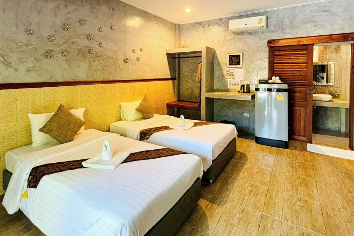A hotel room with two beds, a small kitchenette, a mirror, and a wall-mounted air conditioner.