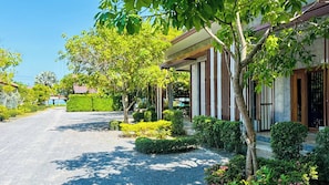 A residential street with a house featuring a covered porch, a driveway, and lush greenery. - Klang Aow Resort (Khanom)
