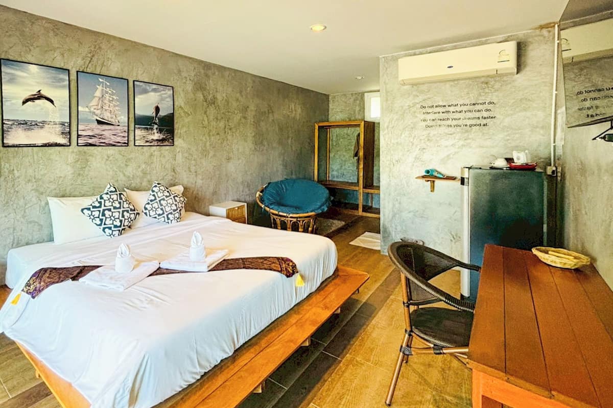 A hotel room with a large bed, a desk, a chair, a mirror, and artwork on the wall.