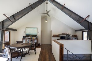 A dining area with a table and chairs, a painting on the wall, and a kitchen area with a counter and shelves. - The Sun Valley Rusty Barn Estate (Hailey)