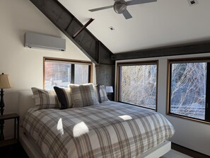 A bedroom with a bed, a ceiling fan, large windows, and a view of trees. - The Sun Valley Rusty Barn Estate (Hailey)