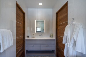 A modern bathroom with a wooden vanity, a large mirror, and a robe hanging on the wall. - The Sun Valley Rusty Barn Estate (Hailey)