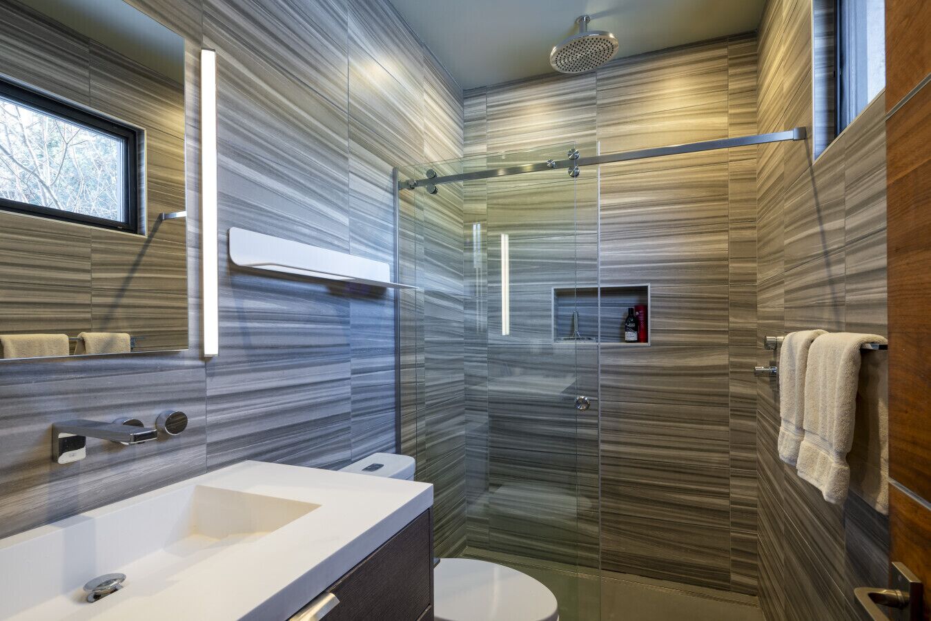 A modern bathroom with a glass shower enclosure, a large mirror, and a vanity with a sink.