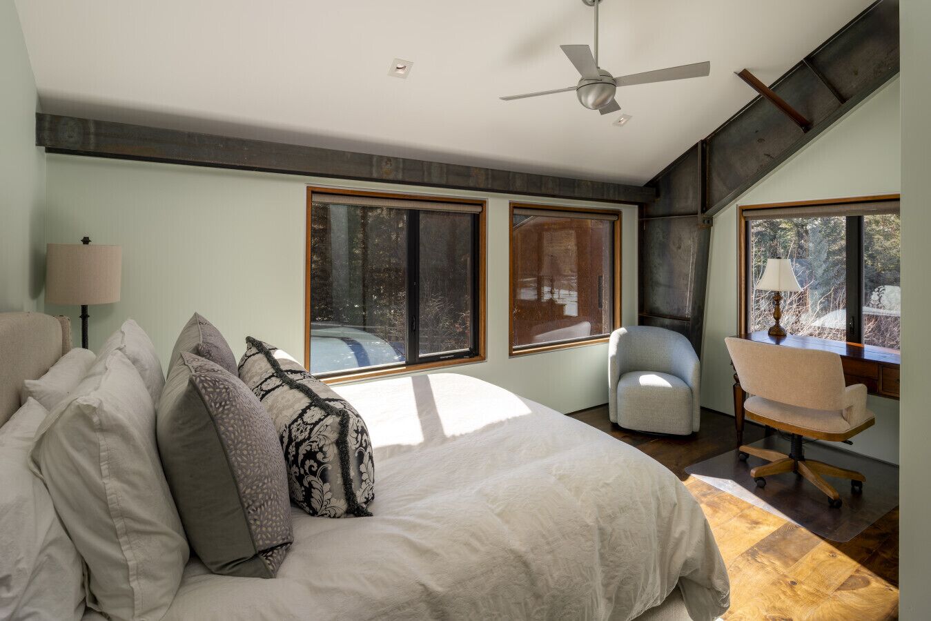 Ein Schlafzimmer mit einem Bett, zwei Fenstern, einem Deckenventilator und einem Stuhl.