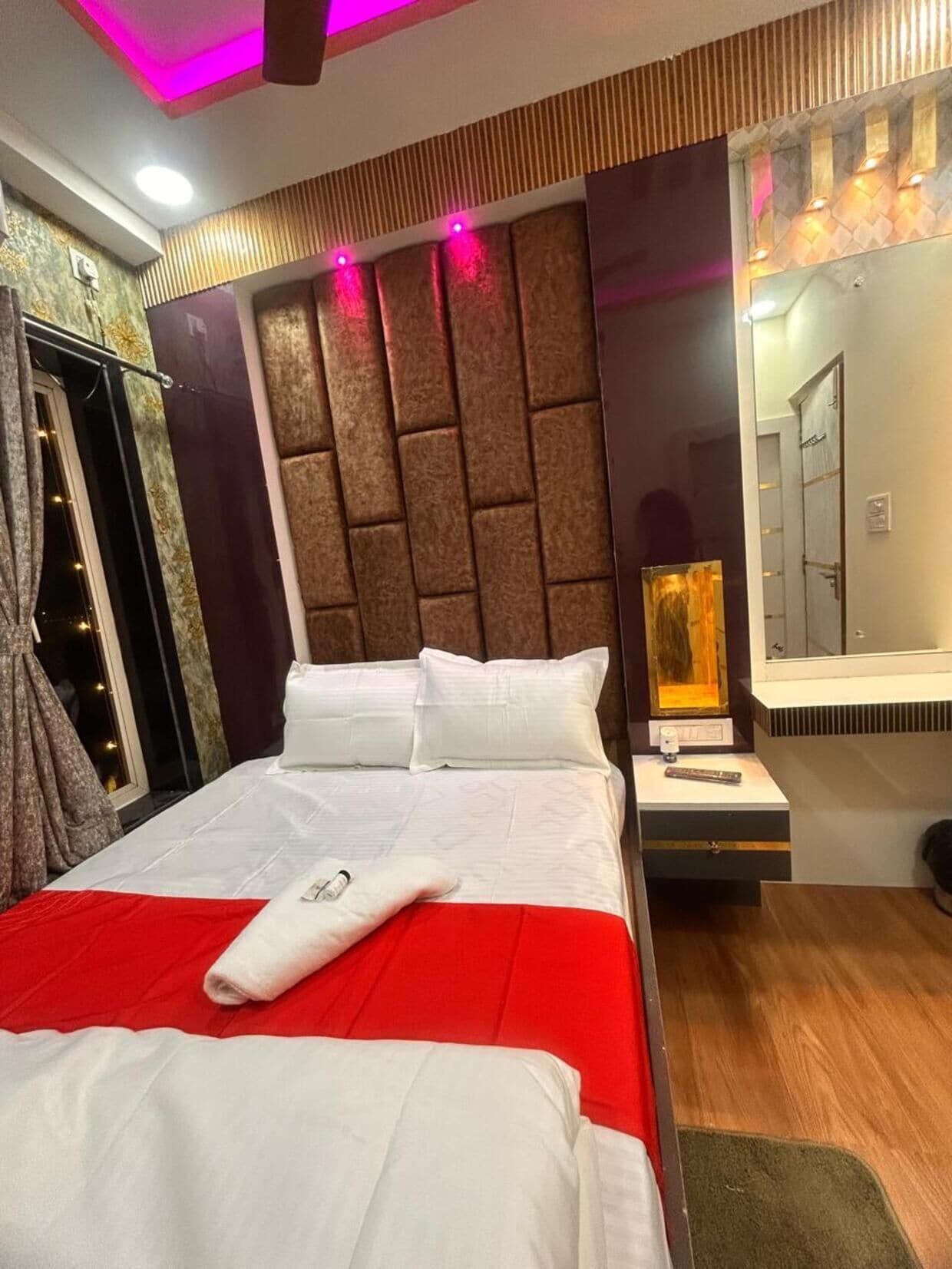 A hotel room with a bed, a nightstand, a mirror, and a window with curtains.