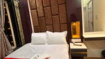 Una habitación de hotel con cama, mesita de noche, espejo y ventana con cortinas.