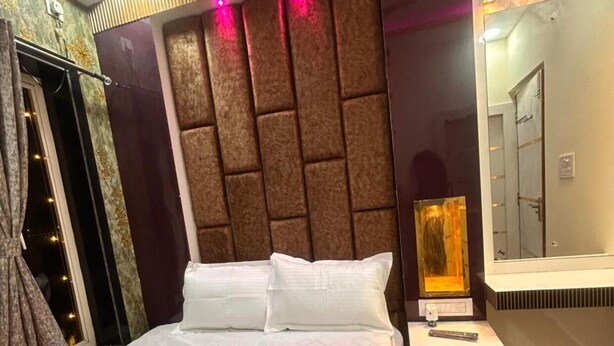 A hotel room with a bed, a nightstand, a mirror, and a window with curtains. - Hotel Runway (Barakpur)