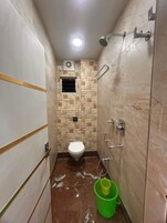 Un baño pequeño con inodoro, ducha y un cubo verde en el suelo.