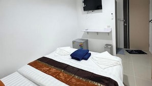 Una camera d'albergo con un letto, una televisione a schermo piatto montata a parete, un comodino e una porta che dà su un'altra stanza.