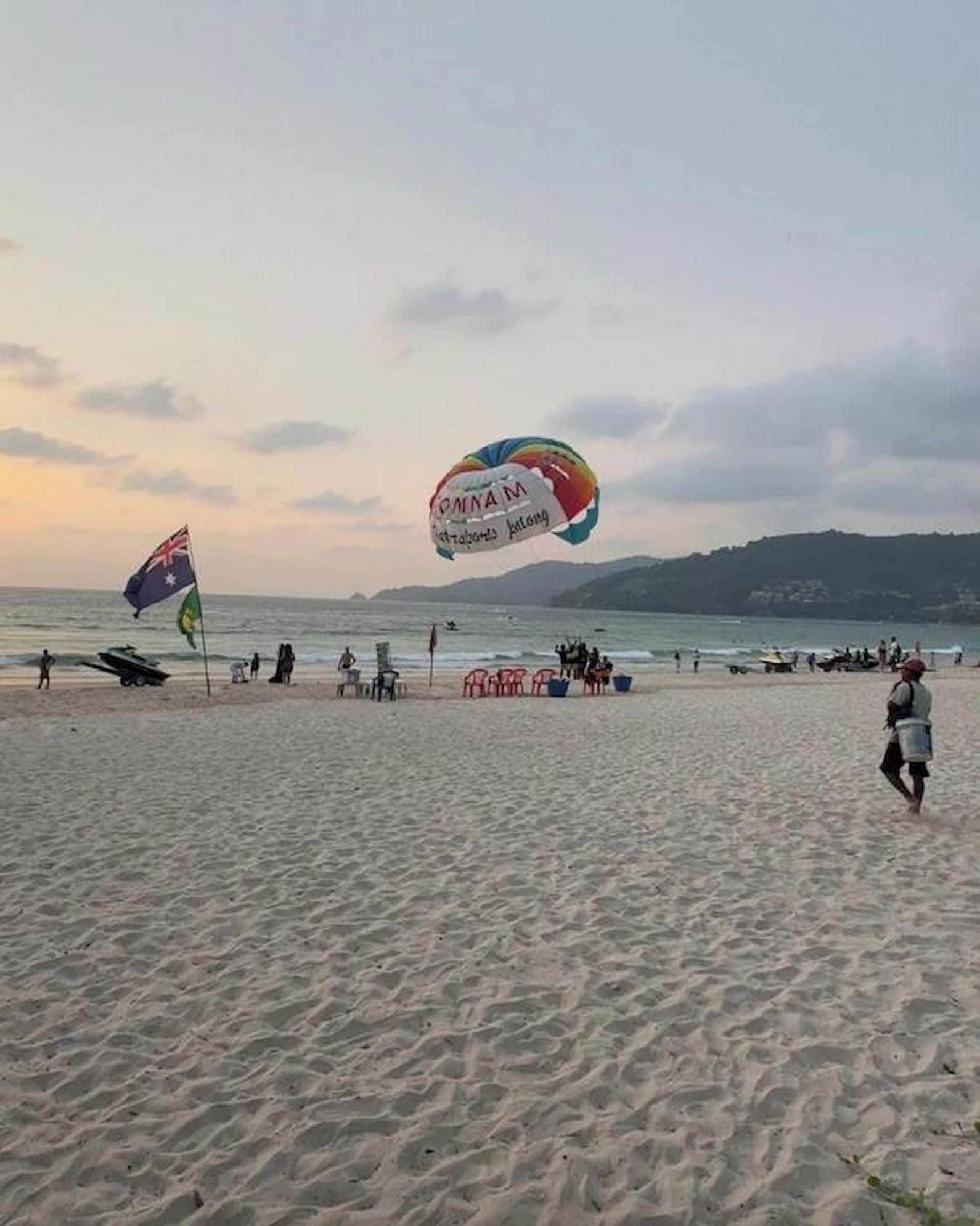 A beach with a large kite and flags, sandy terrain, and a distant shoreline.