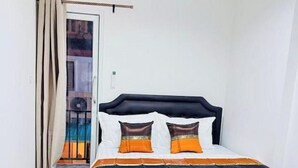 Un letto singolo con una testiera nera, biancheria da letto bianca e due cuscini arancioni.