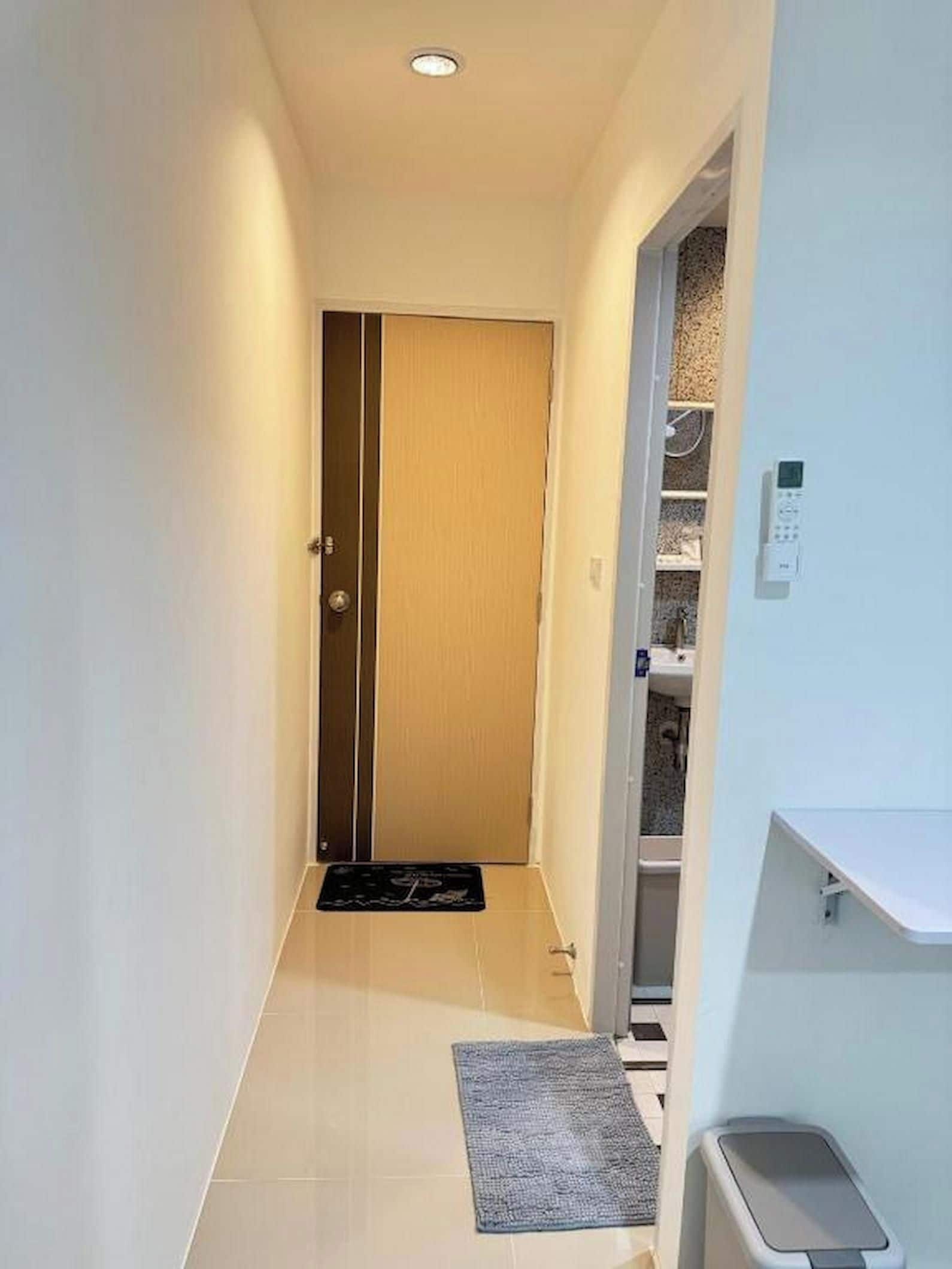 A narrow hallway with a wooden door at the end, a small rug on the floor, and a white trash bin to the right.