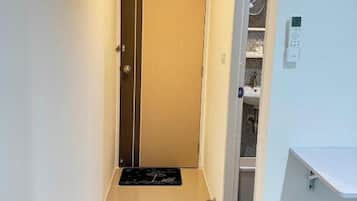 A narrow hallway with a wooden door at the end, a small rug on the floor, and a white trash bin to the right.