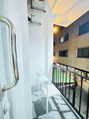 Een balkon met een witte reling, een deur met een metalen handgreep en uitzicht op een gebouw met meerdere ramen.