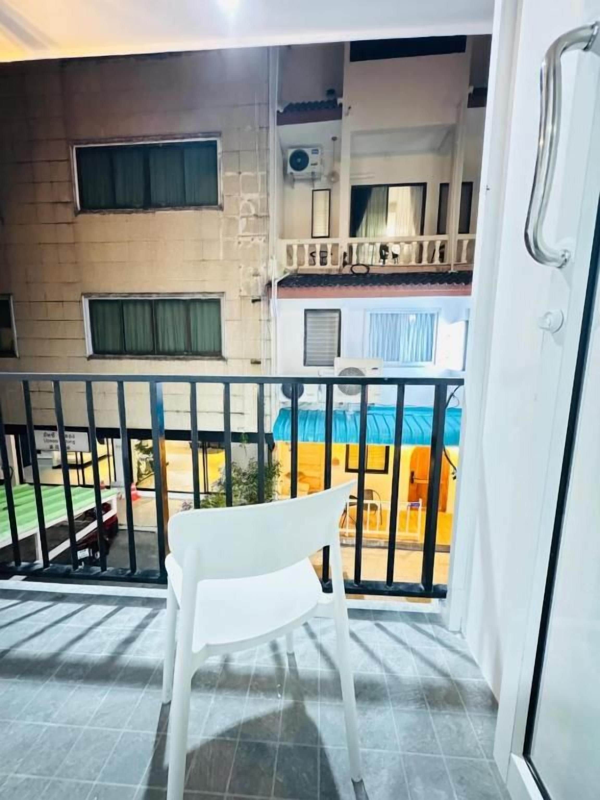 A balcony with a white chair, a metal railing, and a view of a building with multiple windows and balconies.