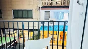 A balcony with a white chair, a metal railing, and a view of a building with multiple windows and balconies.