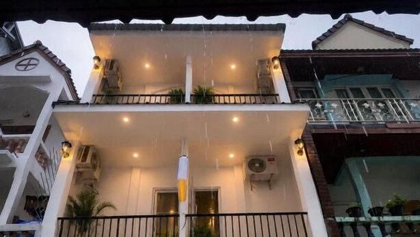 Un edificio a due piani con un balcone, un ingresso coperto e un piccolo spazio esterno con posti a sedere.