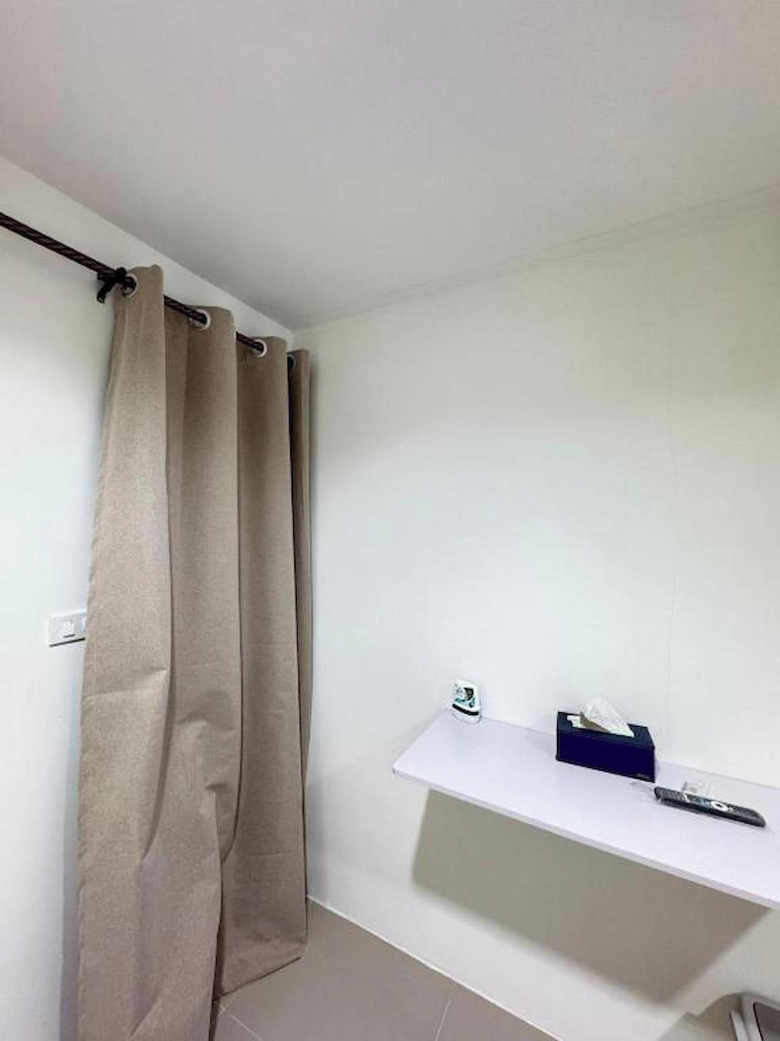 A bathroom with a shower curtain, a white shelf with a tissue box, and a remote control on the floor.